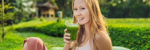 Junge Frau entspannt im Garten und trinkt grünen Smoothie mit Limettenscheibe