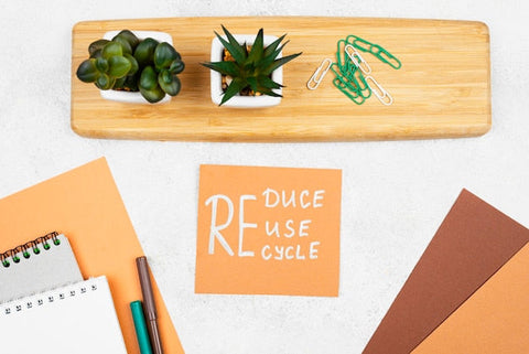Schreibtisch mit Sukkulenten, Büroklammern und Notizzettel mit Aufschrift Reduce Reuse Recycle