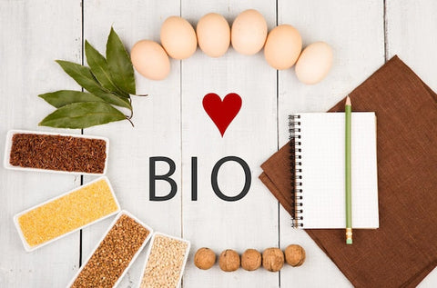 Bio-Lebensmittel wie Eier, Getreide, Nüsse, Lorbeerblätter und Notizblock auf weißem Tisch.