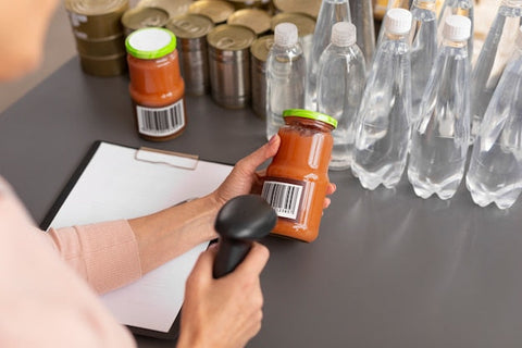 Staff member scans the barcode on a jar of tomato sauce, water bottles, tins and stock