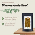 Pflanzenhaarfarbe warmes Honigblond Packung auf Holztisch mit Produktbeschreibung und Blättern.